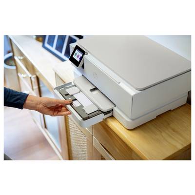 Eine Person legt ein Dokument in den Papierschacht eines weißen Druckers in einem hell erleuchteten Raum. Der Drucker verfügt über ein kleines digitales Display.