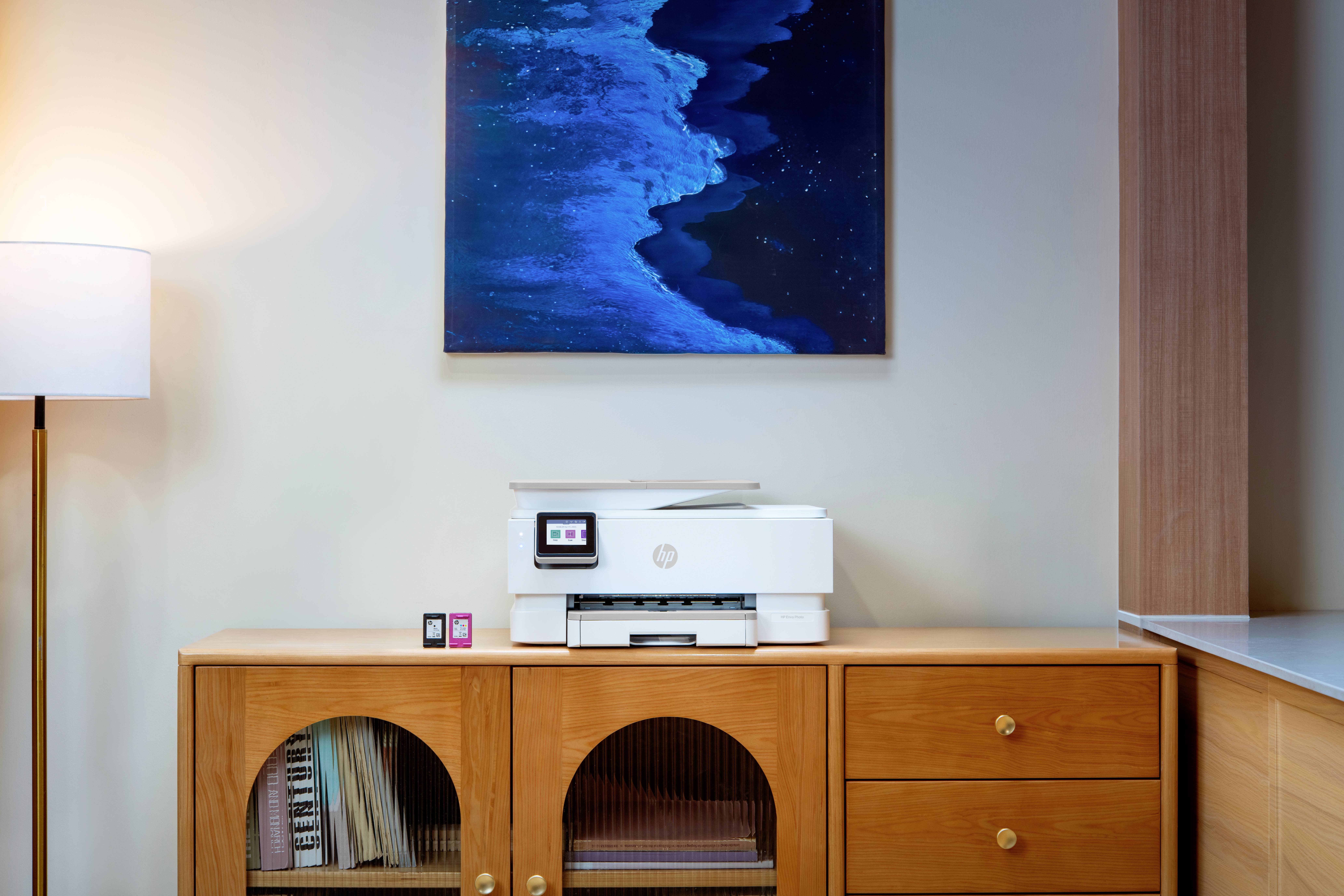 Ein moderner Home-Office-Bereich zeigt einen Holzschrank mit einem Drucker und kleinen Fotorahmen, unter einem blauen abstrakten Gemälde.