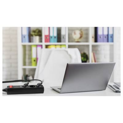 Laptop auf einem Schreibtisch mit einer Steckdosenleiste, vor Regalen mit bunten Ordnern und einem Globus, was ein Home-Office-Setup andeutet.