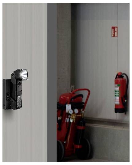 Eine Taschenlampe, die an einer Wand befestigt ist, beleuchtet einen Brandschutzbereich mit einem hängenden Feuerlöscher und einem mobilen Feuerwagen in der Nähe.