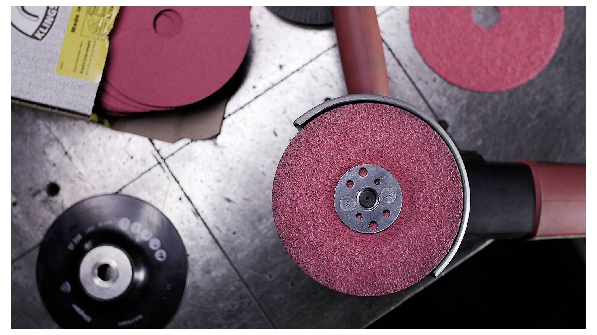 'Eine Nahaufnahme einer roten Winkelschleifer mit einer neuen Schleifscheibe auf einer metallischen Werkbank, umgeben von zusätzlichen Scheiben und Verpackungen.'