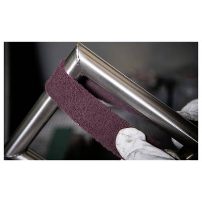 Zwei Hände mit Handschuhen polieren einen Metallrahmen mit einem dunkelroten Schleifstreifen und verbessern dessen Glanz und Oberfläche.