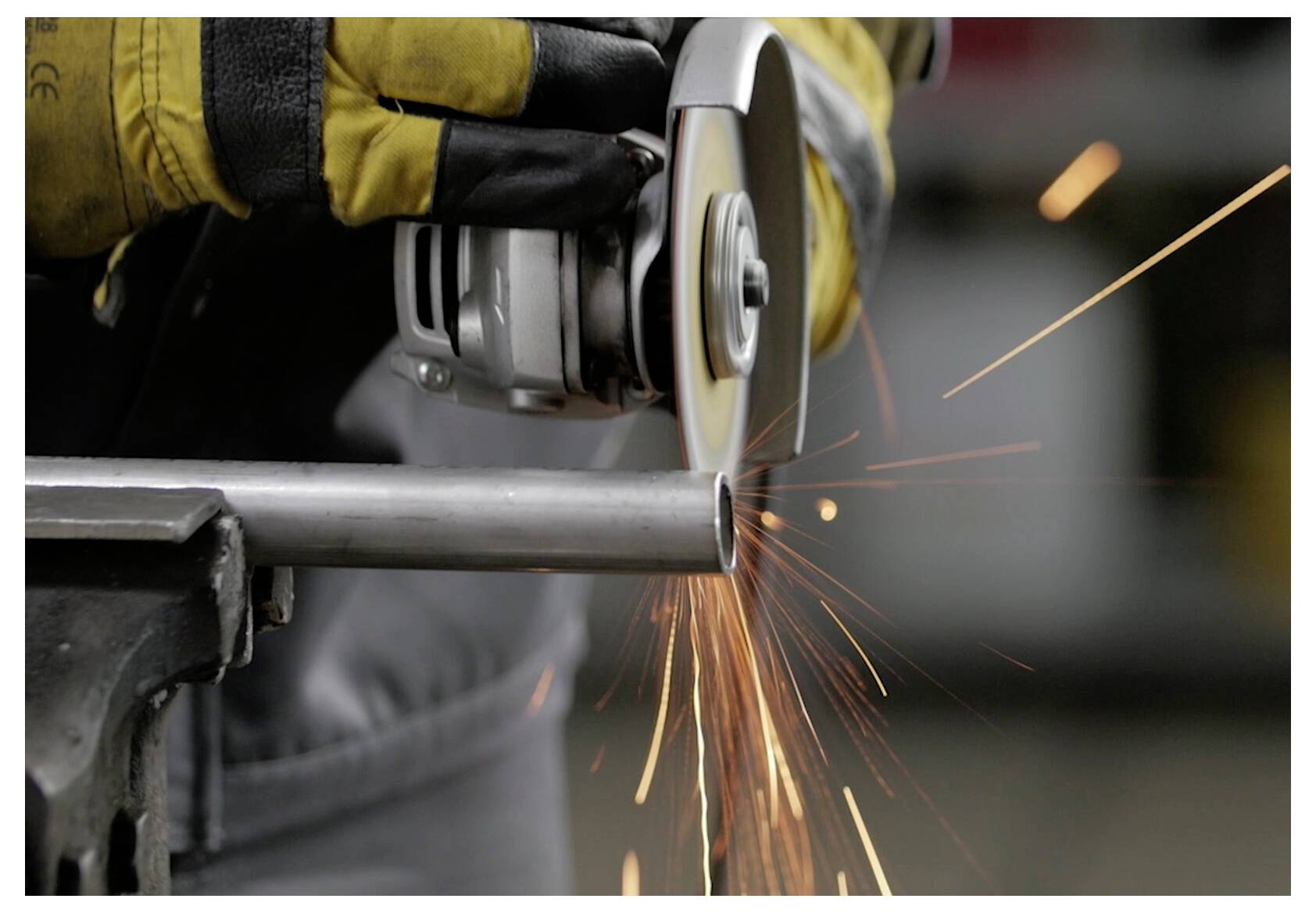 Eine Person mit Schutzhandschuhen verwendet eine Winkelschleifer, um ein Metallrohr zu durchtrennen, wobei Funken an der Kontaktstelle sprühen.