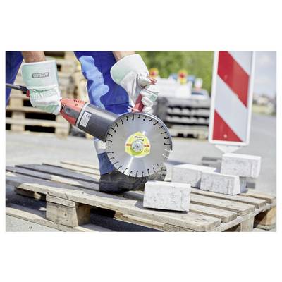 Eine Person in Arbeitskleidung verwendet eine Elektrosäge, um Betonblöcke auf einer Holzpalette auf einer Baustelle zu schneiden.