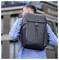 Eine Person mit einer Jeansjacke trägt einen großen schwarzen Rucksack mit einem Logo auf dem Rücken und steht vor einem modernen Gebäude.