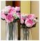 Eine Vase mit rosa und weißen künstlichen Blumen auf der linken Seite und leuchtend rosa Rosen mit Blattwerk auf der rechten Seite, getrennt durch eine vertikale Linie.