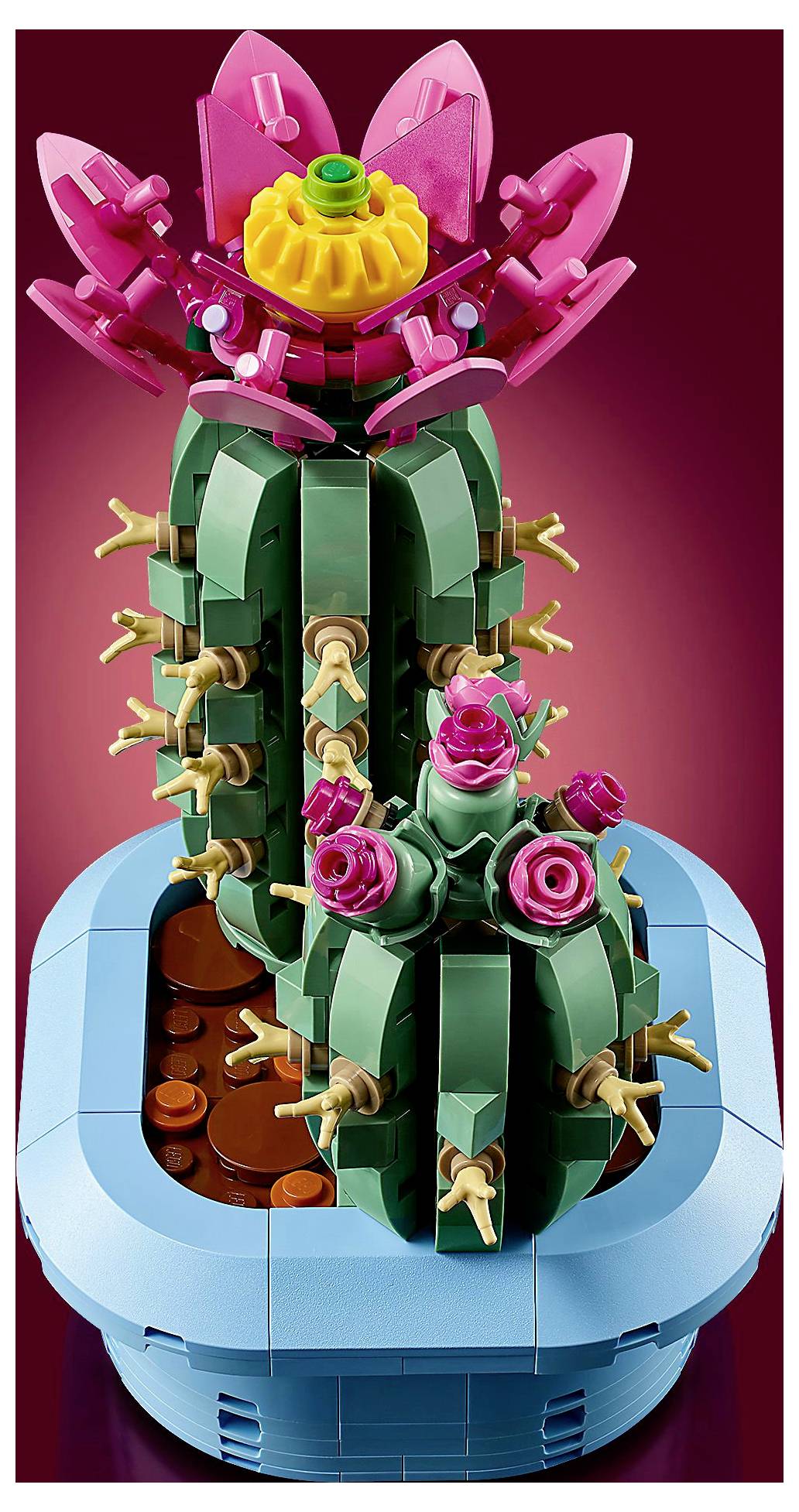 Ein LEGO-Modell von zwei grünen Kakteen mit rosa und gelben Blüten in einem blauen Topf vor einem Verlaufshintergrund in Rosa.