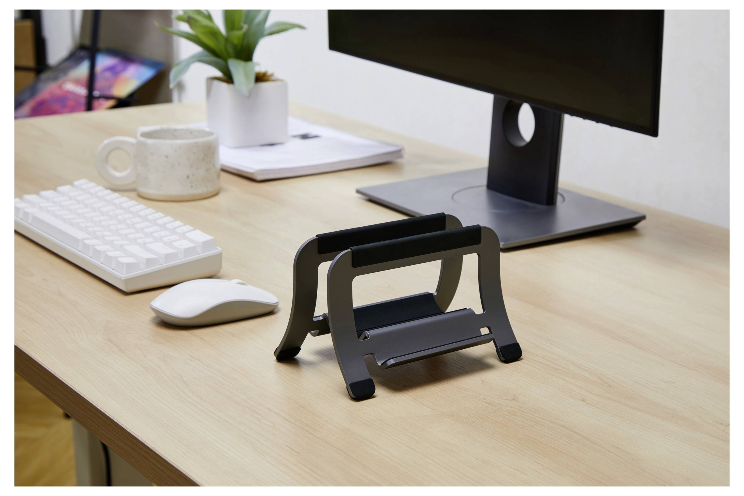 Ein Schreibtischaufbau mit einem Computermonitor, einer Tastatur, einer Maus, einer Pflanze und einer Doppel-Laptop-Halterung auf einer Holzschreibtischoberfläche.