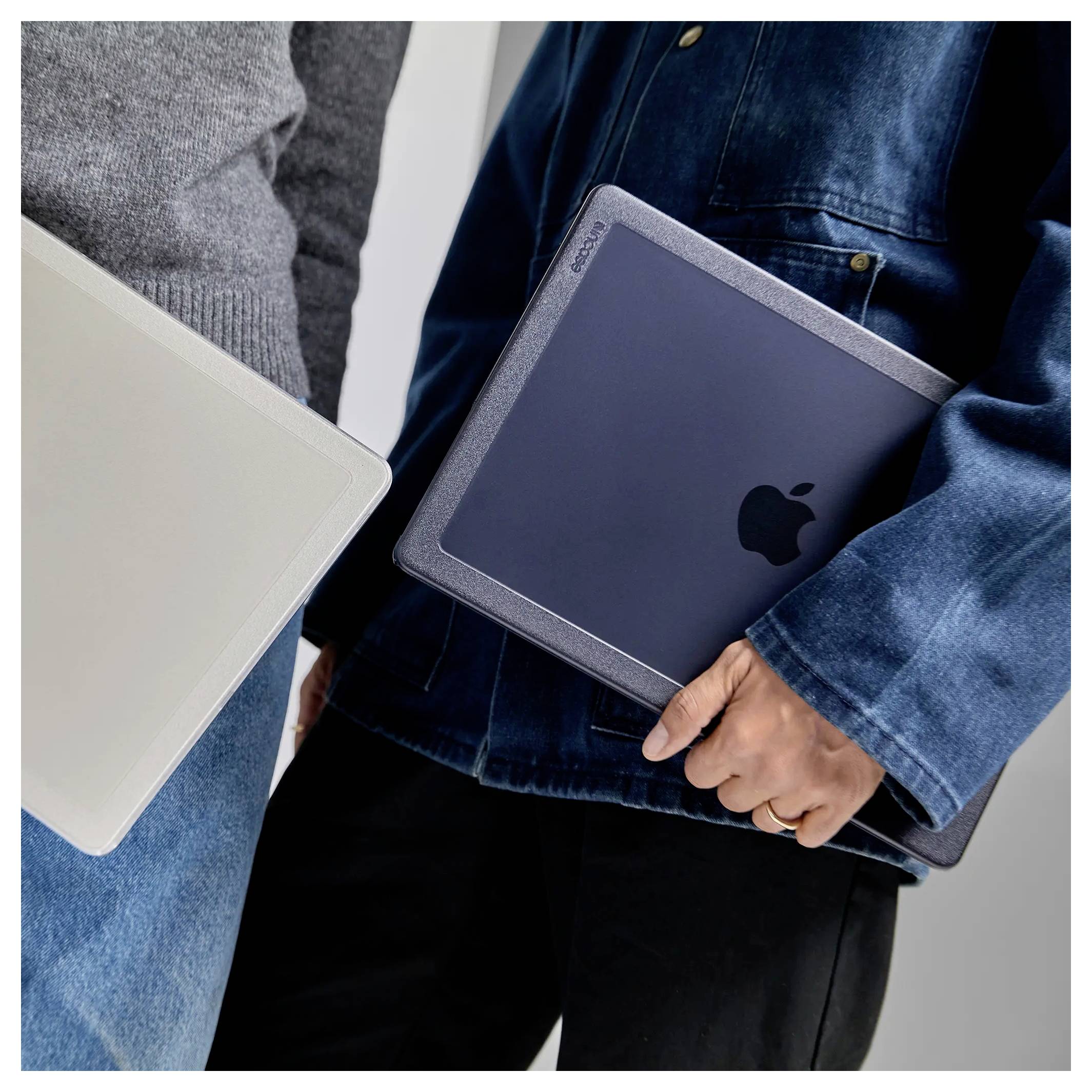 Zwei Personen, die geschlossene Laptops halten, einer mit einem Apple-Logo, tragen lässige Jacken.