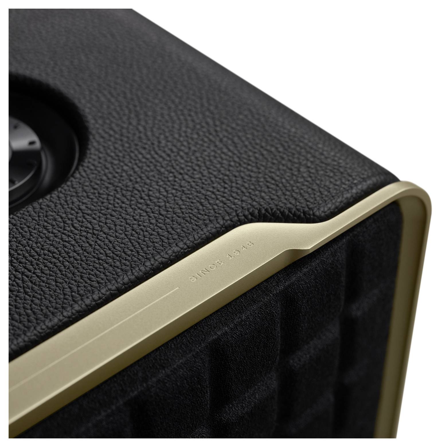 Nahaufnahme einer Lautsprecher-Ecke mit schwarzer Lederstruktur und einer goldenen Akzentprägung mit der Aufschrift ‚SEIT 1946'; das Lautsprechergitter ist sichtbar.