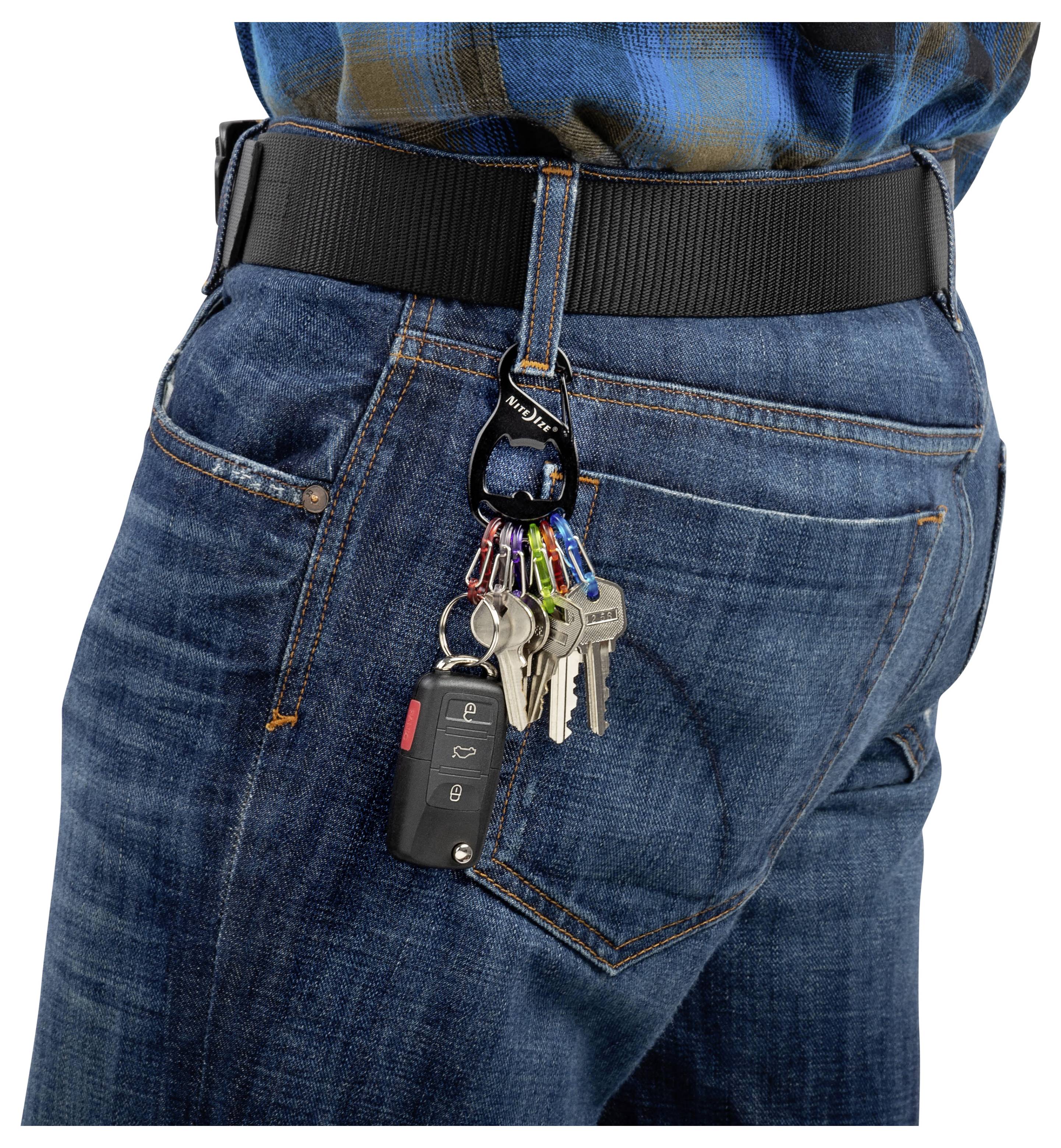 Eine Person trägt Jeans mit einem schwarzen Gürtel, an dessen Gürtelschlaufe ein Schlüsselanhänger befestigt ist. Der Schlüsselanhänger trägt mehrere Schlüssel und eine Autoferndedienung.
