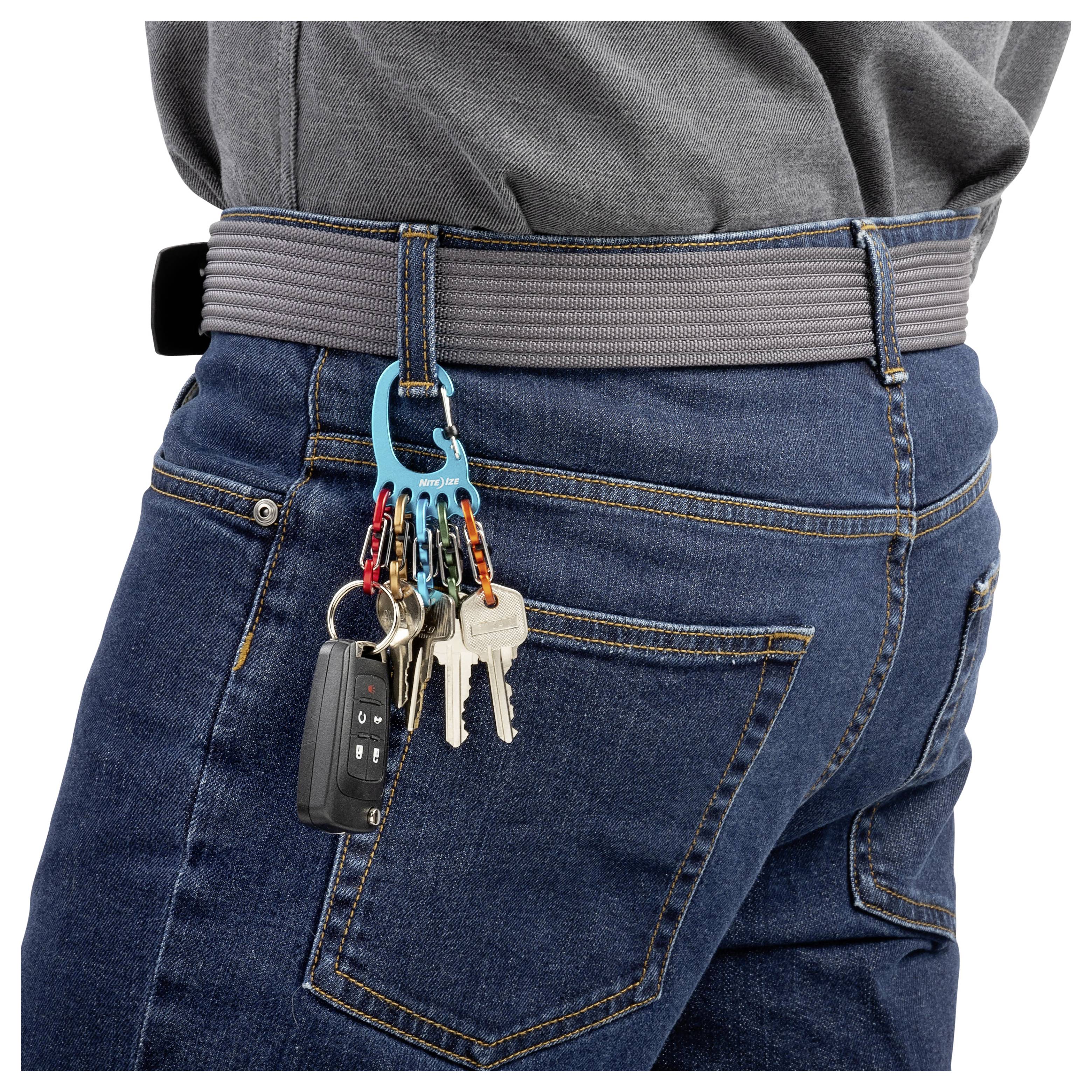 Eine Person trägt Jeans und einen grauen Gürtel und hat einen Schlüsselanhänger mit mehreren Schlüsseln und einer Autoferntastatur, der an der Gürtelschlaufe befestigt ist.