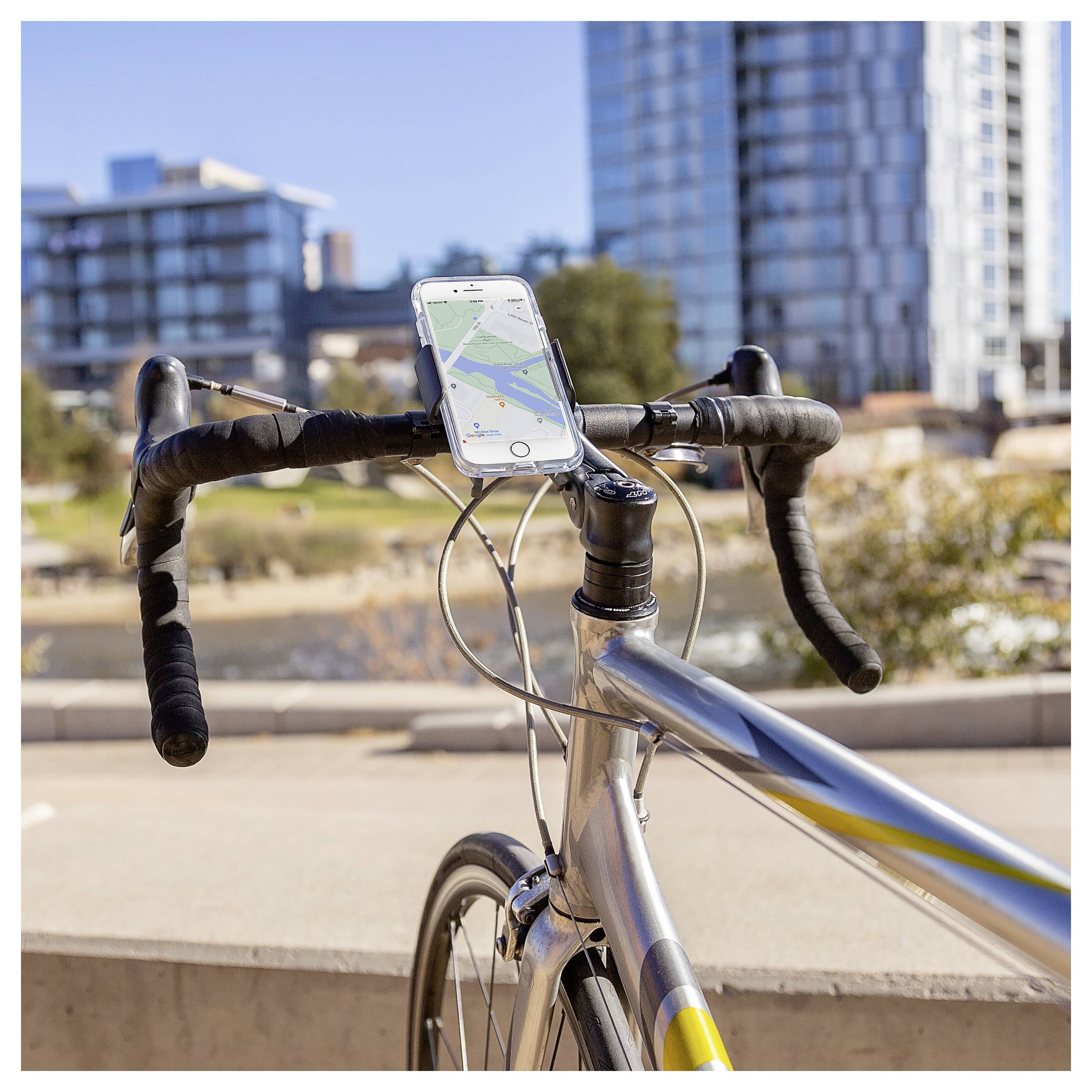 Ein Rennrad mit einem Smartphone, das am Lenker befestigt ist und eine Navigationskarte anzeigt. Städtische Gebäude und ein Park sind im Hintergrund sichtbar.