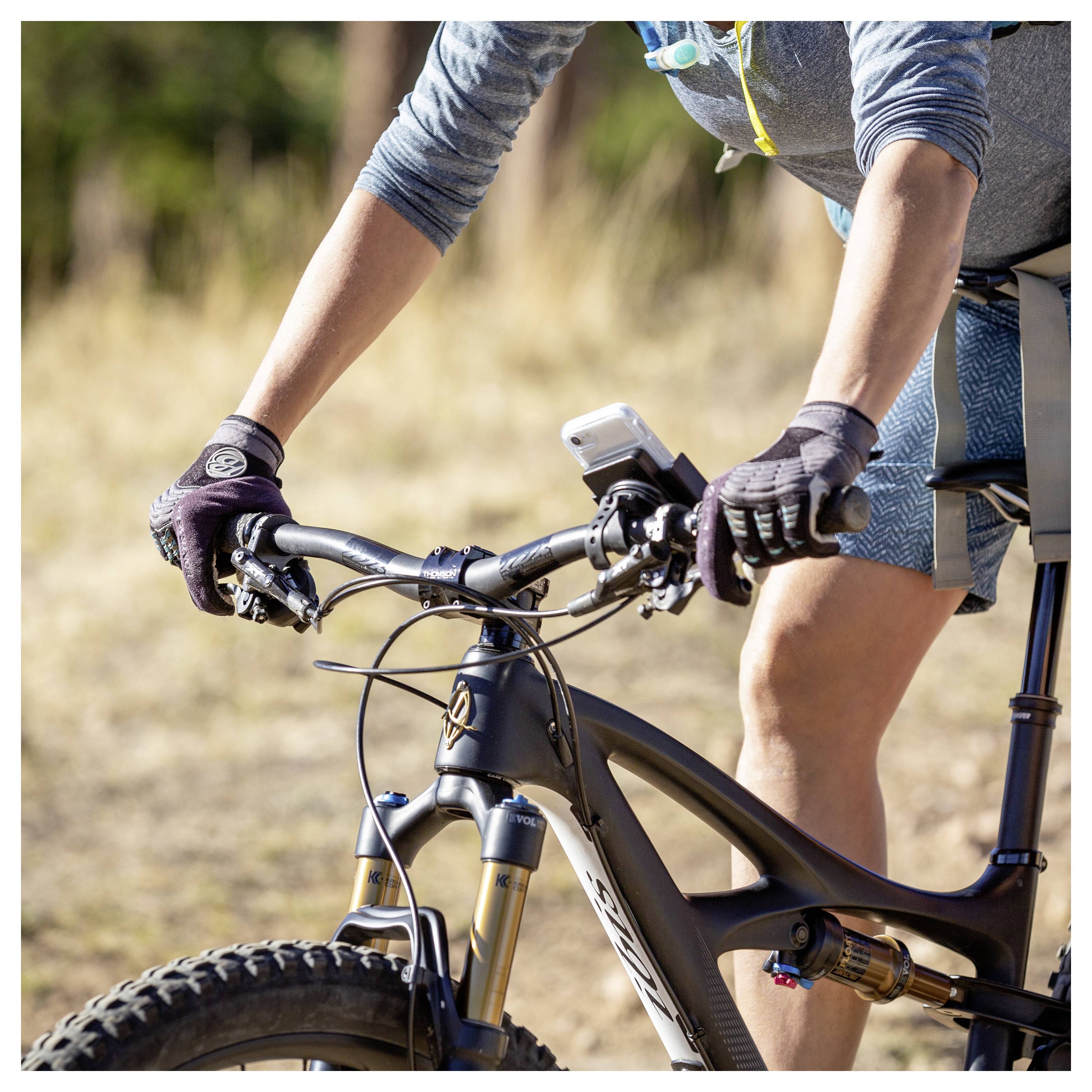 Eine Person auf einem Fahrrad auf einem Pfad, trägt Handschuhe und eine blaue Sportbekleidung, umklammert die Lenkstange. Der Hintergrund zeigt unscharf verschwommene Vegetation und einen Weg.