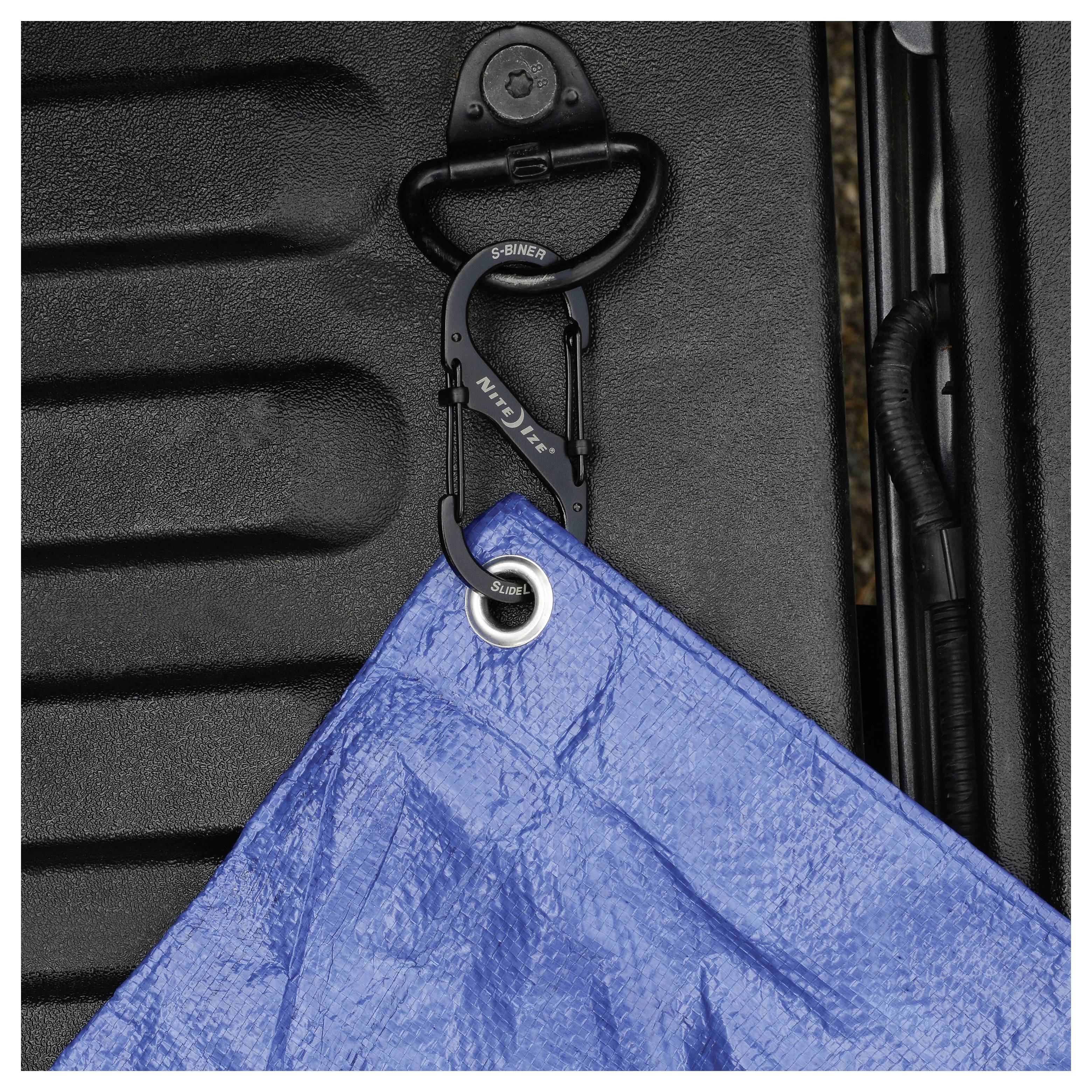 Eine blaue Plane, die mit einem schwarzen Karabiner auf einer strukturierten Oberfläche befestigt ist; verwendet zum Abdecken oder Schützen von Gegenständen.
