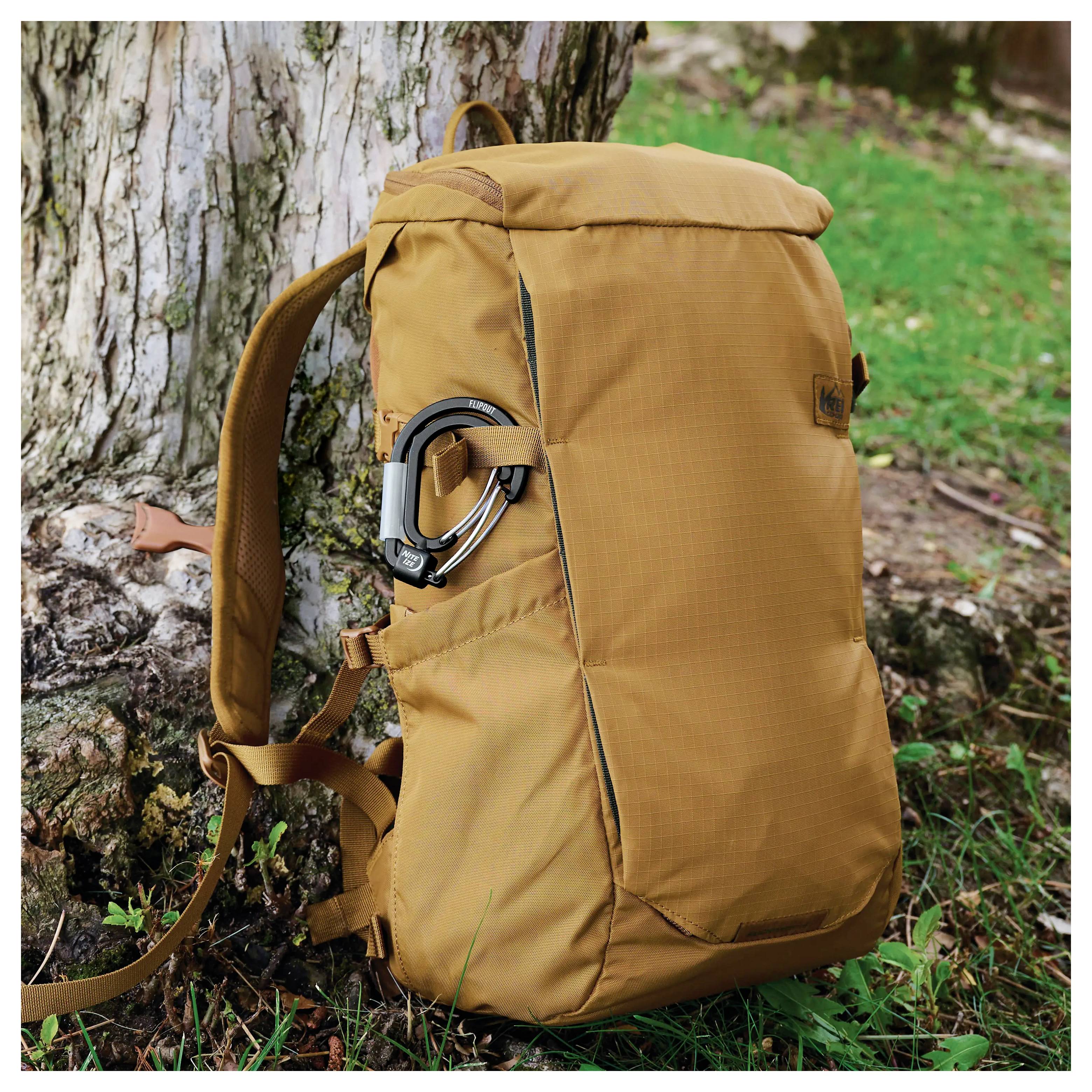 Ein gelber Rucksack mit einem Karabinerhaken, der an einen Baumstamm angelehnt auf einer Grasfläche ruht.