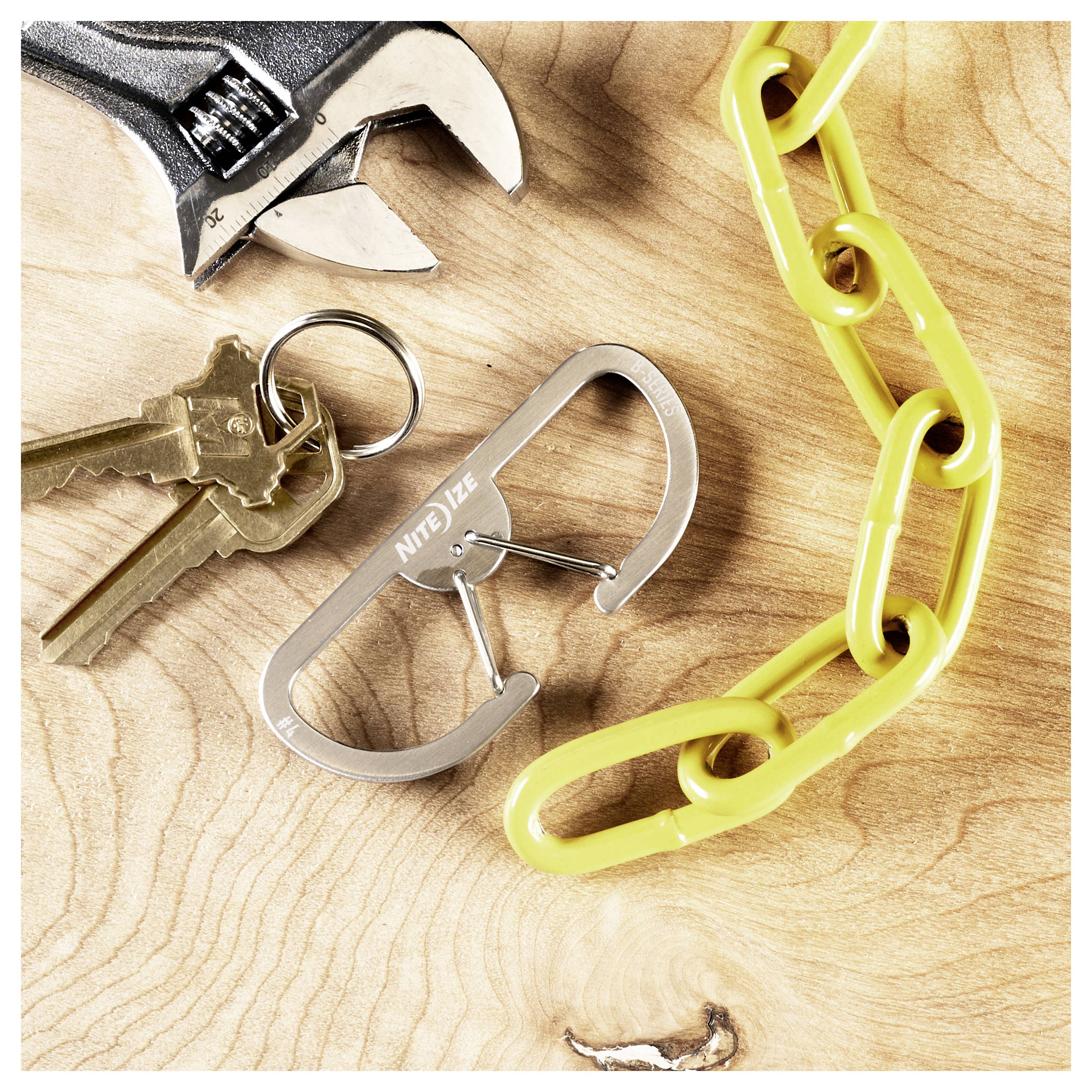 Schlüssel und ein Metallkarabiner der Marke 'Nite Ize' auf einer Holzoberfläche, neben einem Schraubenschlüssel und gelben Kunststoff-Kettengliedern.