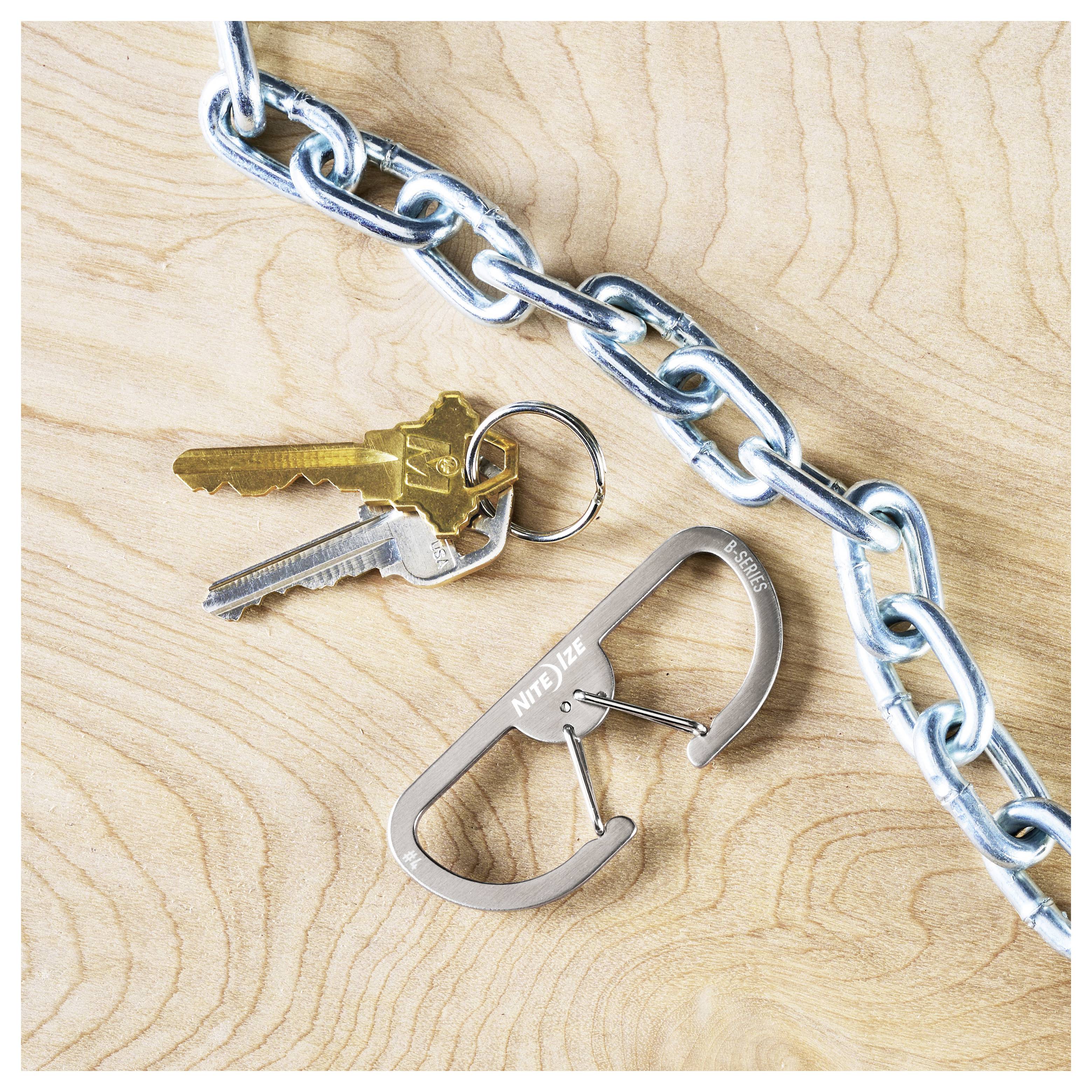 Ein Paar Schlüssel, die an einer Metallkette mit einem Karabiner auf einer Holzoberfläche befestigt sind. Der Karabiner ist mit dem Schriftzug "Nite Ize" graviert.