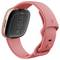 Eine roséfarbene Smartwatch mit quadratischem Zifferblatt und einem Herzfrequenzsensor auf der Rückseite, auf der der Markenname "Fitbit" zu sehen ist.
