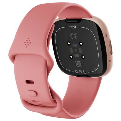 Eine roséfarbene Smartwatch mit quadratischem Display und Armband, die gedreht ist, um ihre verschiedenen Sensoren zur Gesundheitsüberwachung und den Markennamen zu zeigen.