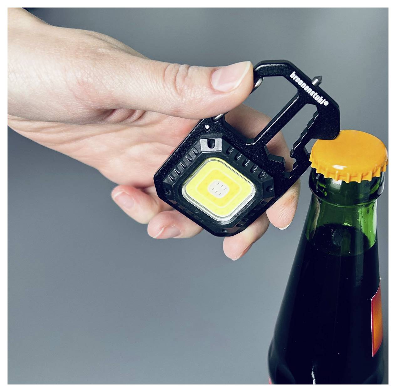 Eine Hand verwendet ein schwarzes Multitool mit einem gelben Licht, um eine Flasche mit einem orangefarbenen Deckel zu öffnen.