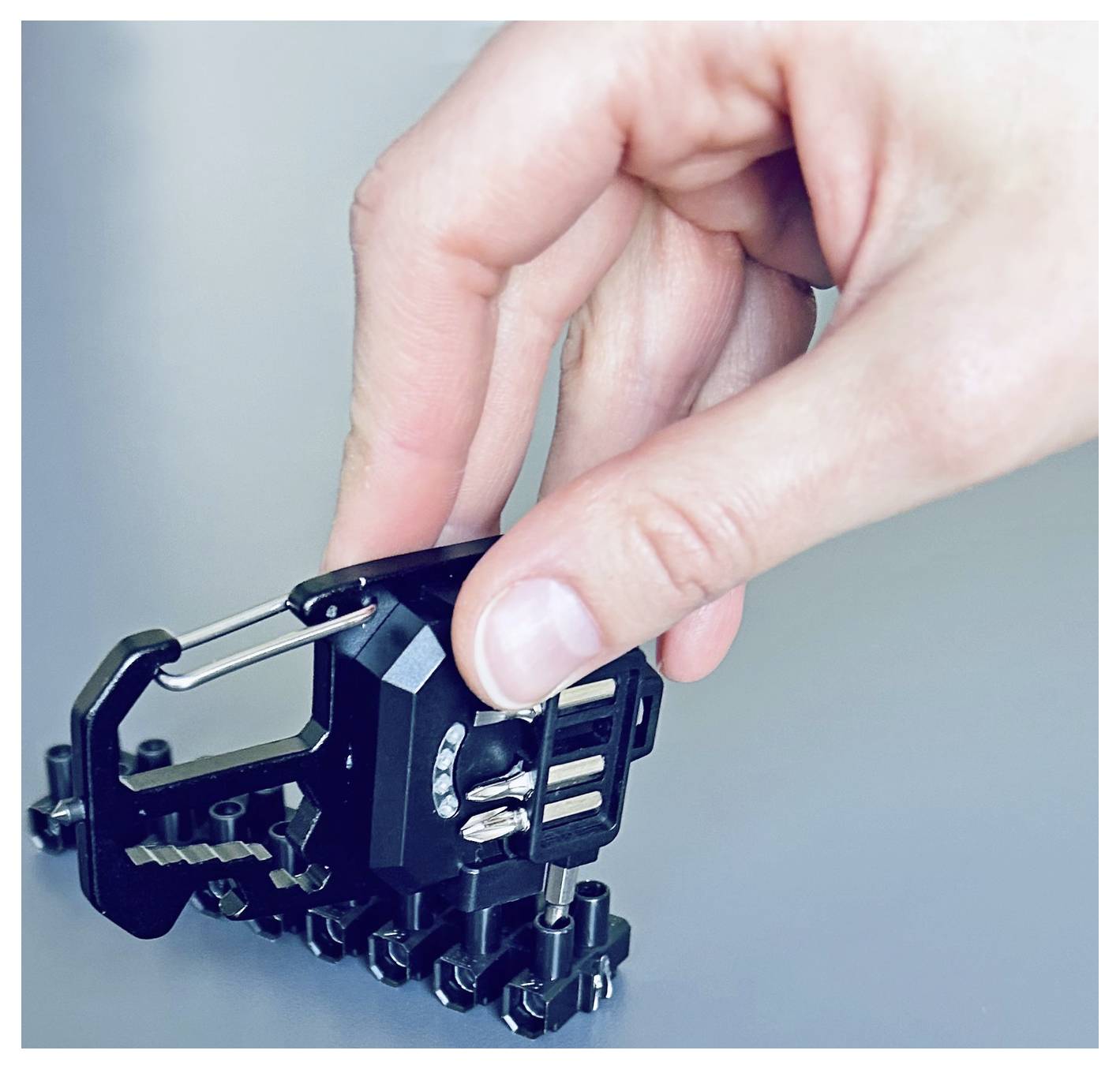 Eine Hand justiert ein kleines schwarzes mechanisches Werkzeug auf einer grauen Oberfläche und demonstriert dessen Funktionalität.