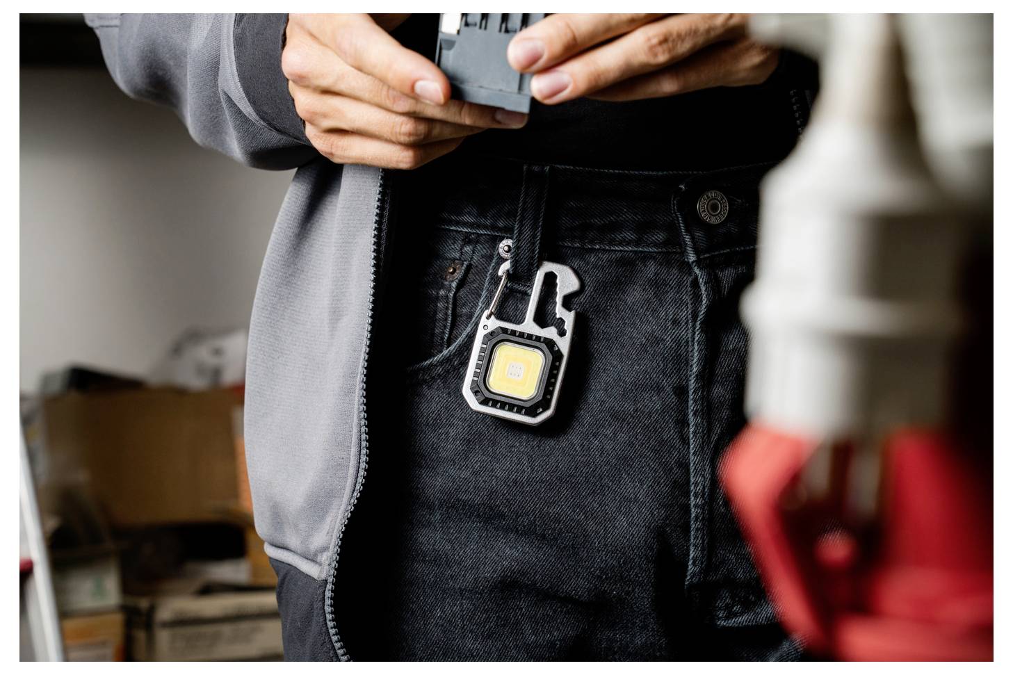 Eine Person, die ein kleines Werkzeug über einer Tasche mit einer anklippbaren LED-Lampe hält und sich in einer Werkstattumgebung befindet.