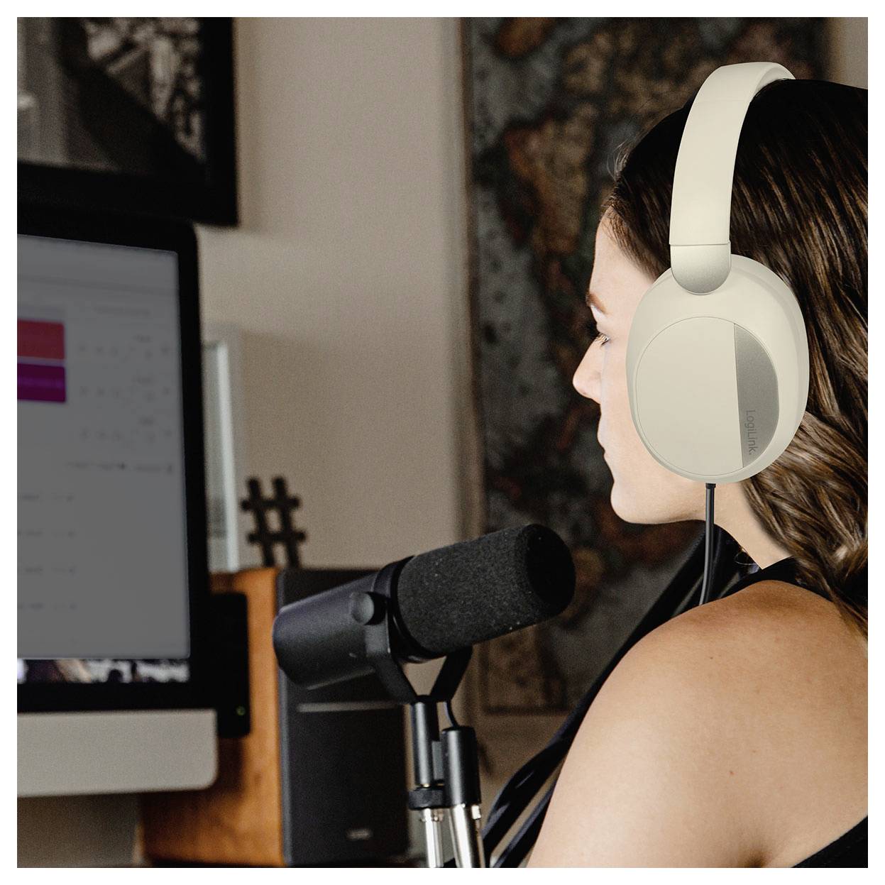 Eine Person mit Kopfhörern spricht in ein Mikrofon und nimmt Audio an einem Schreibtisch auf, wobei ein Computerbildschirm im Hintergrund sichtbar ist.