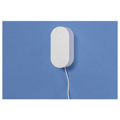 Eine weiße, an einer blauen Wand montierte elektronische Vorrichtung mit einem herabhängenden Kabel, möglicherweise ein Smart-Home-Hub oder Sensor.
