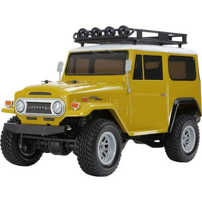 Ein Vintage-Geländewagen in Gelb mit Dachgepäckträger und großen Reifen, von schräg vorne links betrachtet.