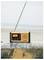 Ein gelbes tragbares Radio mit ausgefahrener Antenne steht auf einer Betonbarriere am Strand. Das Display zeigt '97.4'.