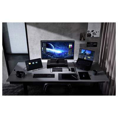 Ein moderner Arbeitsbereich mit einem großen Monitor, der eine Science-Fiction-Landschaft zeigt, zwei Laptops links und rechts, einem Grafiktablett und einer Tastatur.