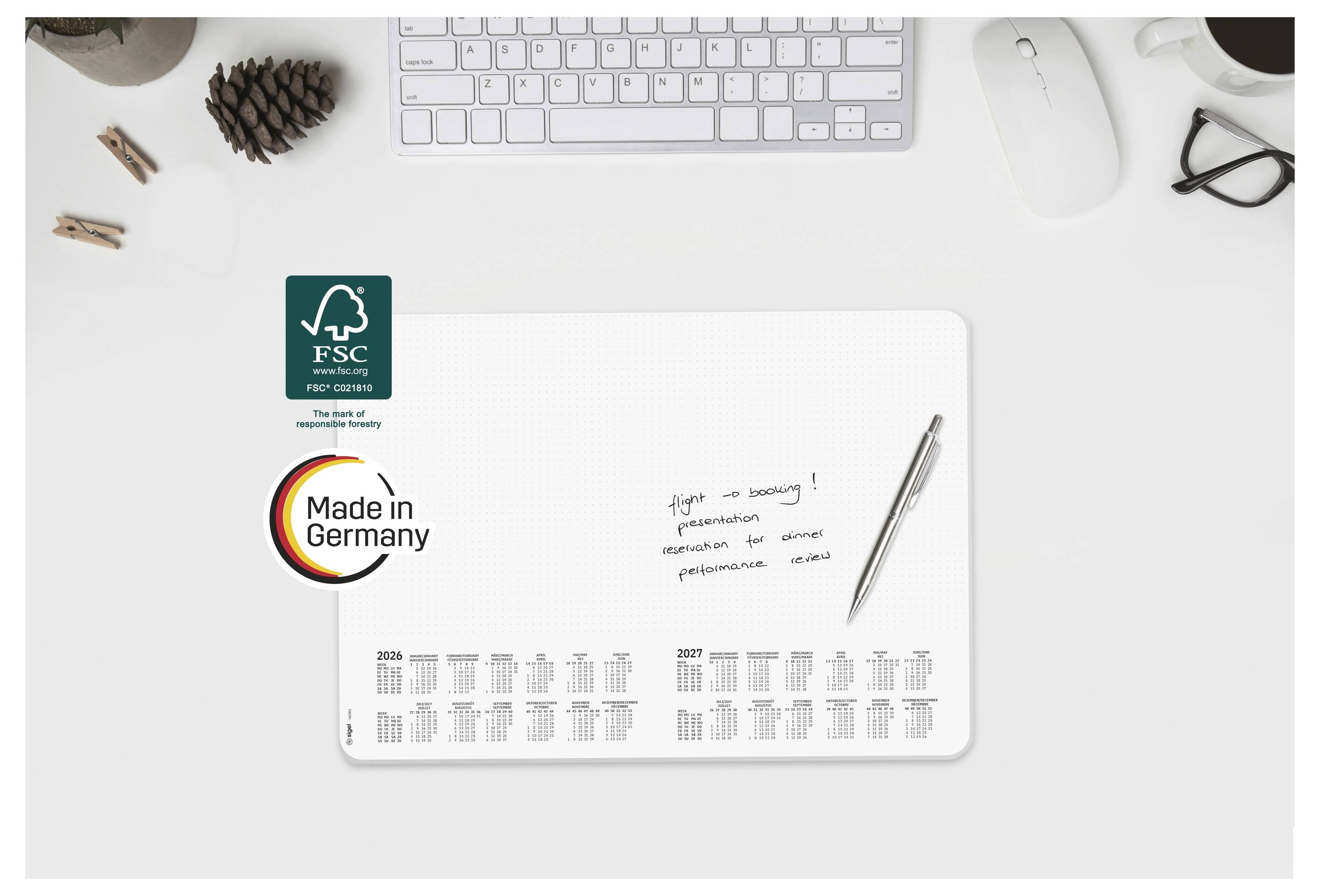 Desktop-Mockup eines Marken-Papierplaners mit FSC- und „Made in Germany"-Etiketten, einem Stift, einer Tastatur, einer Maus, einer Brille und Bürozubehör.
