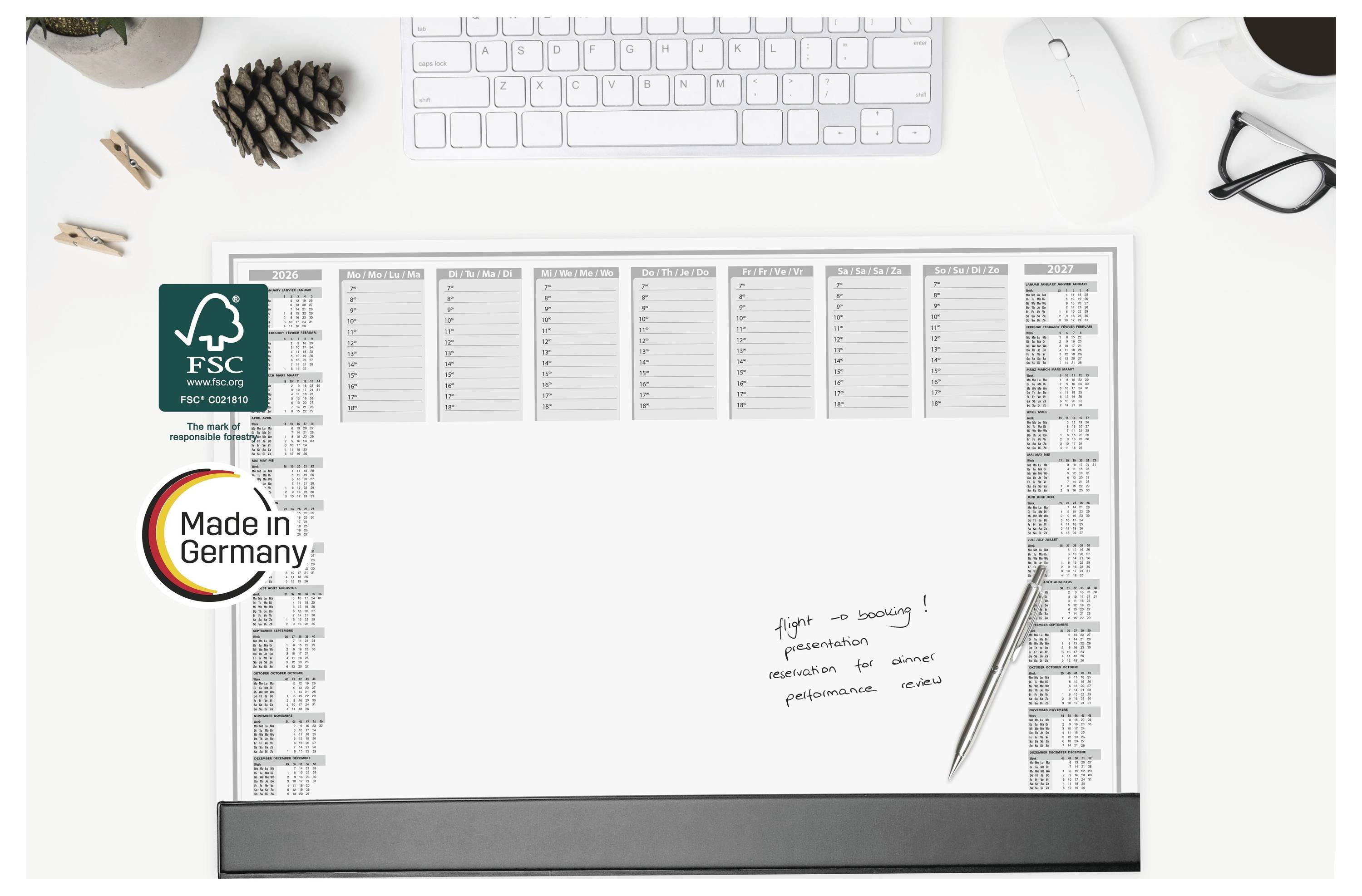 Tischkalender/Planer auf weißem Schreibtisch mit FSC- und „Made in Germany"-Logos; Tastatur, Maus, Brille und Stift in der Nähe.