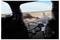 Blick von der Rückseite eines Autos, der ein Fahrradrad, einen Helm und Ausrüstung vor einer Straße zeigt, die sich in die Wüstenlandschaft unter einem blauen Himmel erstreckt.