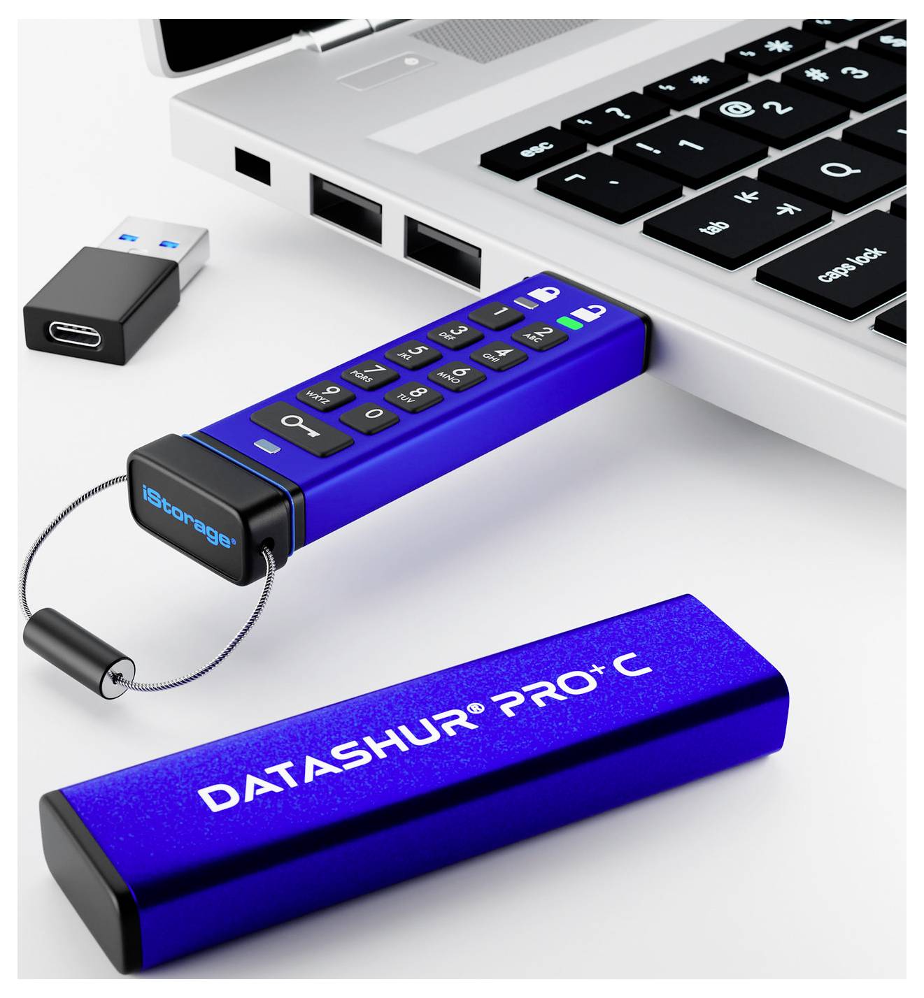 Ein blauer USB-Stick mit Tastatur, beschriftet mit 'datAshur PRO+C', ist in einen Laptop eingesteckt. Ein weiteres USB-Gerät befindet sich in der Nähe.