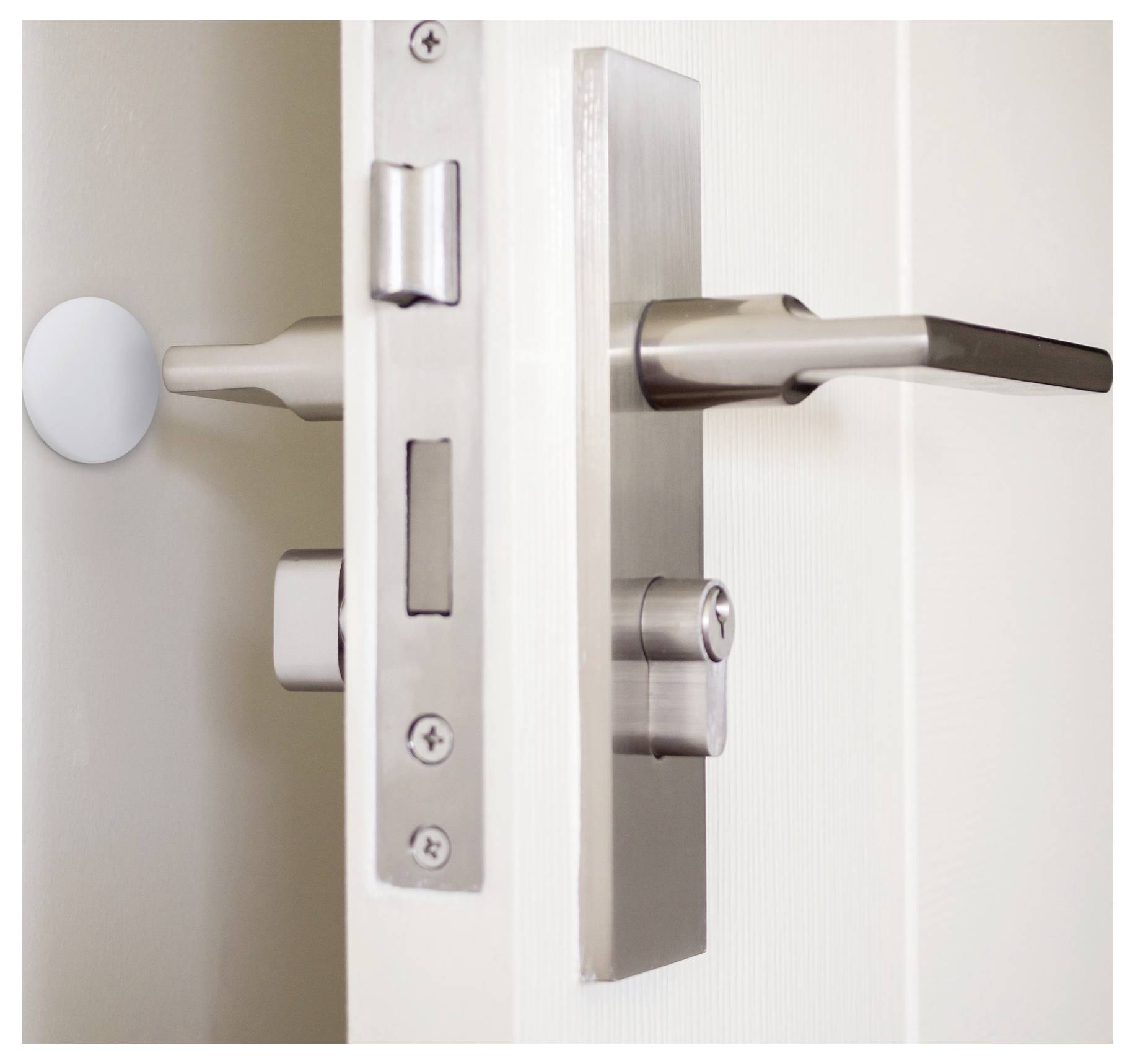 Grauer Metalltürgriff und Schloss an einer leicht geöffneten weißen Tür, von der Seite betrachtet, mit modernem Design und klaren Linien.