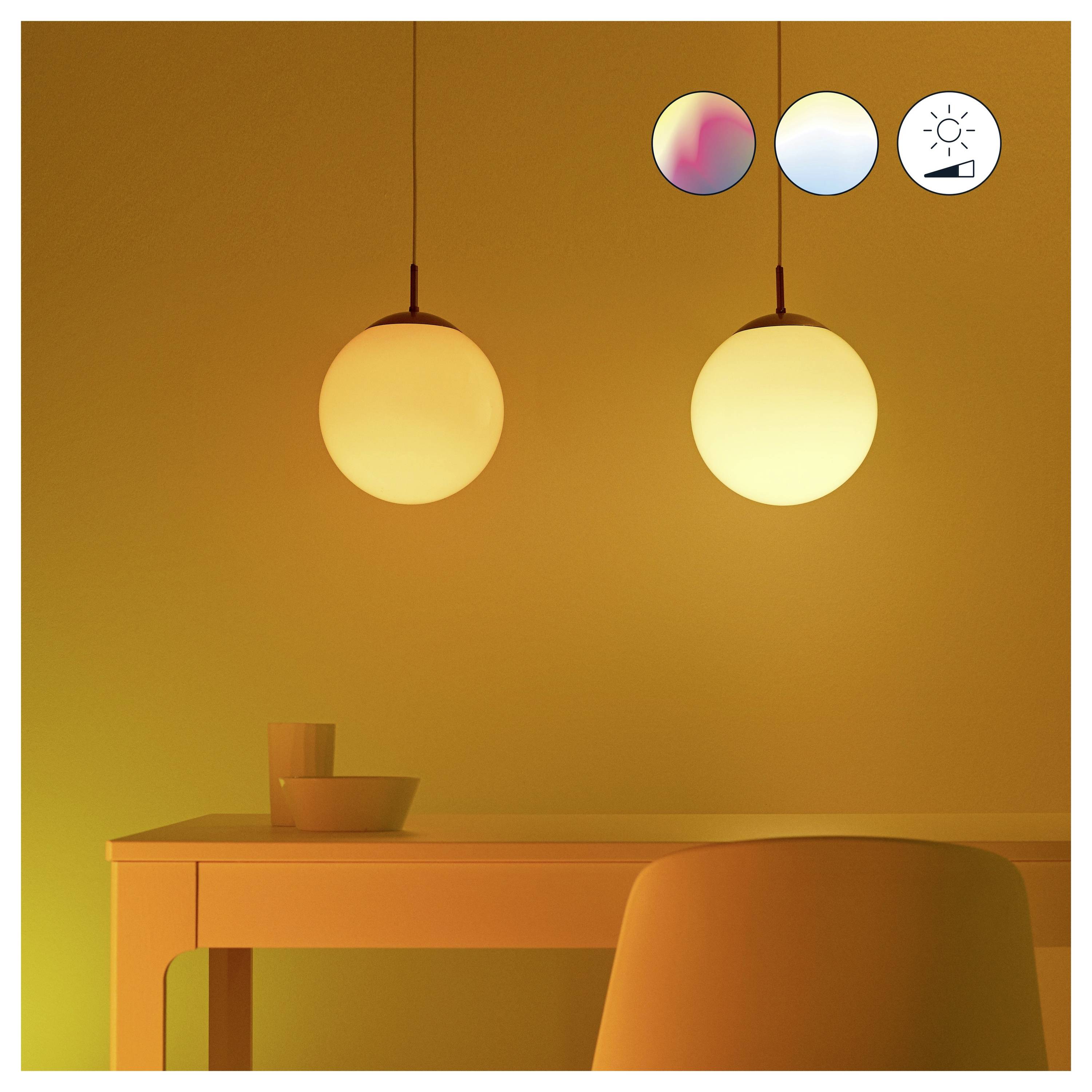 Ein warmer, ambient beleuchteter Raum mit zwei hängenden kreisförmigen Lampen über einem Tisch und Stuhl. Symbole zeigen die Einstellbarkeit von Lichtfarbe und Helligkeit an.