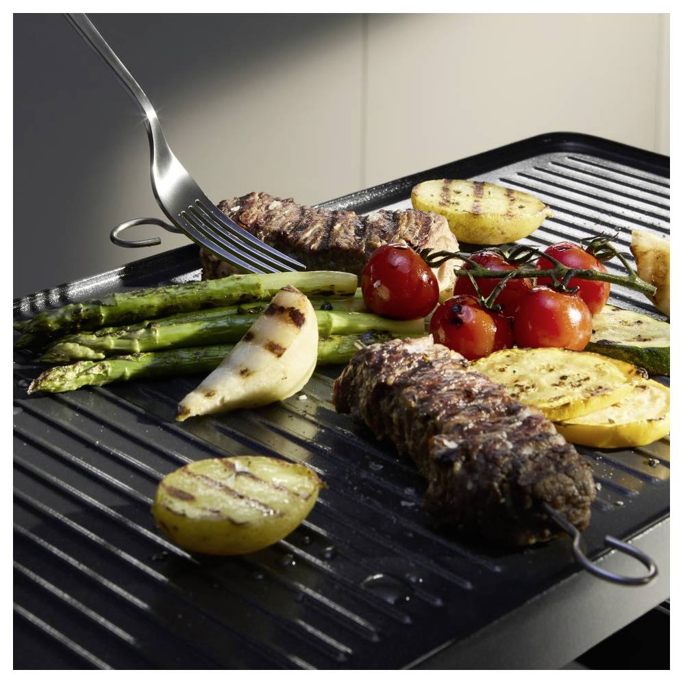 Gegrilltes Fleisch und Gemüse, einschließlich Spargel, Kartoffelscheiben, Tomaten und Zwiebeln, in einer gerippten Grillpfanne mit einer Gabel darauf.