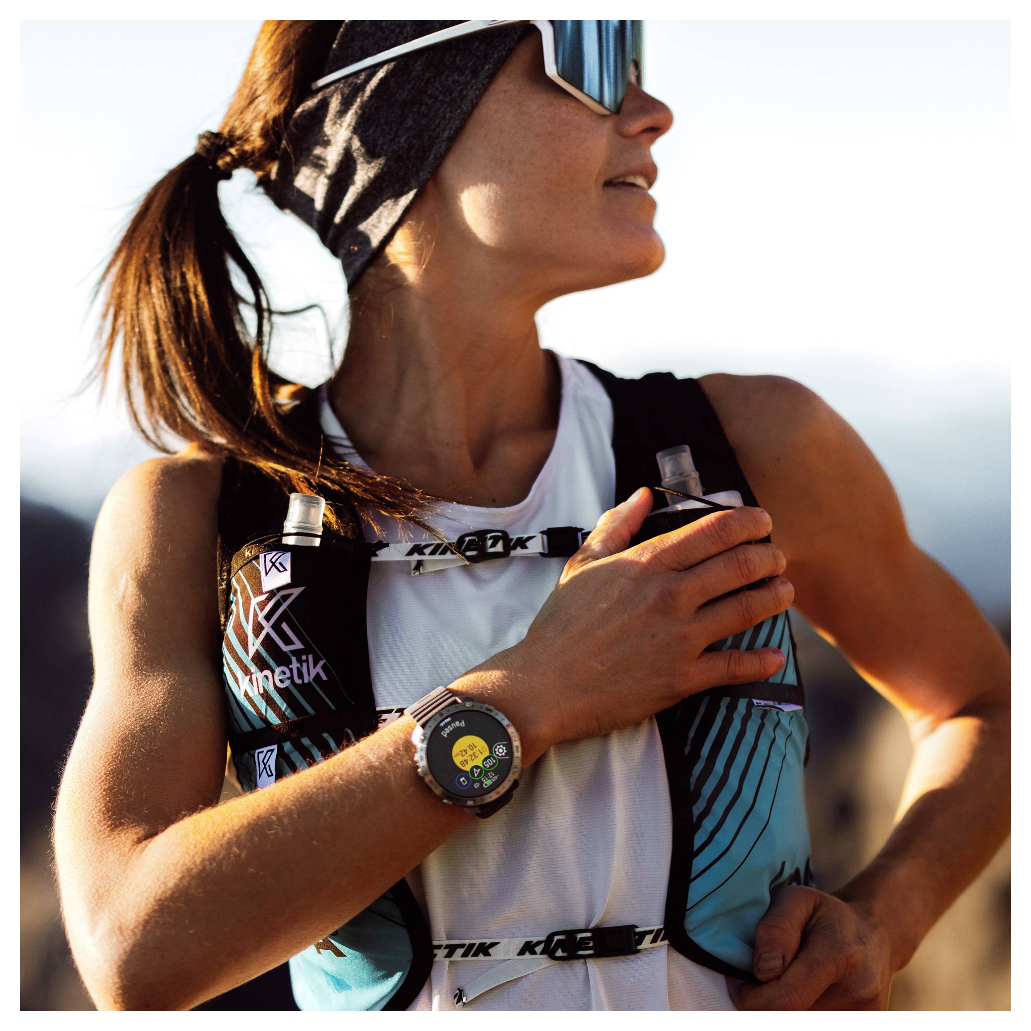 Eine Person im Freien mit einem Stirnband und Sonnenbrille, die nach oben schaut und einen Fitness-Tracker einstellt. Die Szene deutet auf Sport oder Abenteuer hin.