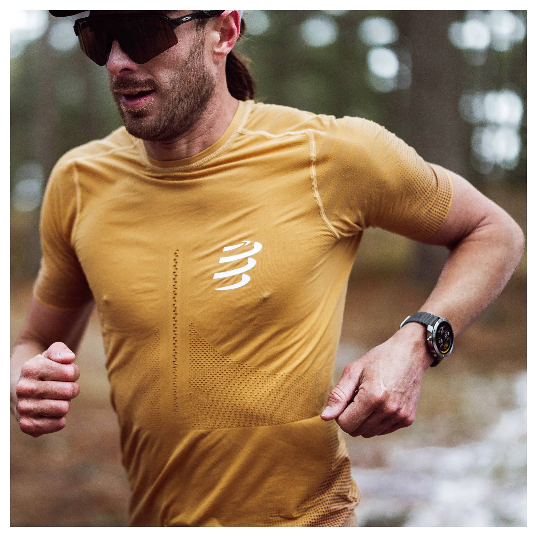 Eine Person, die in einem Wald läuft, trägt ein gelbes Sportshirt, Sonnenbrille und eine Smartwatch, mit entschlossenem Blick nach vorn gerichtet.