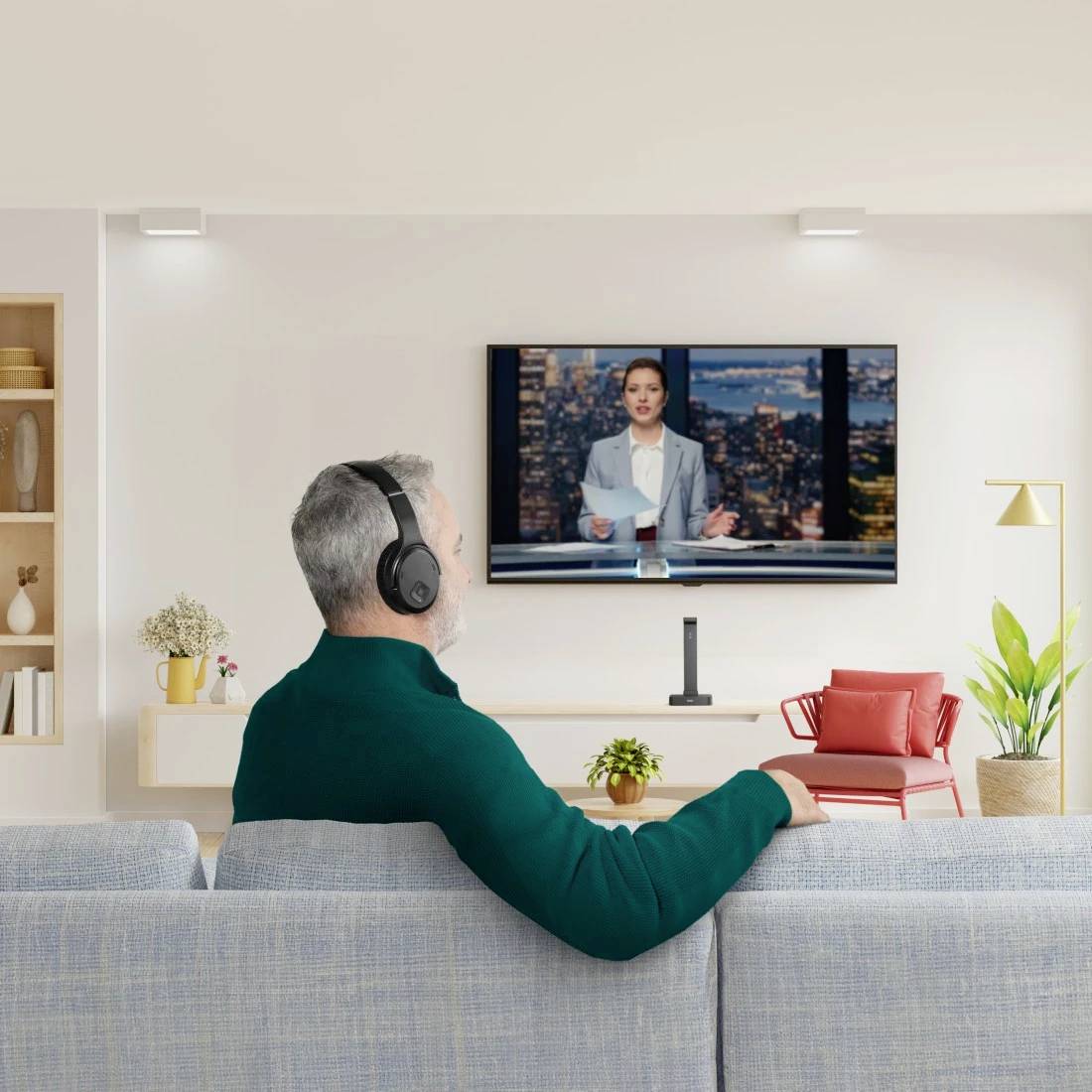 Eine Person mit Kopfhörern sitzt auf einem Sofa und schaut eine Nachrichtensendung auf einem an der Wand montierten Fernseher in einem modernen, hell beleuchteten Wohnzimmer.