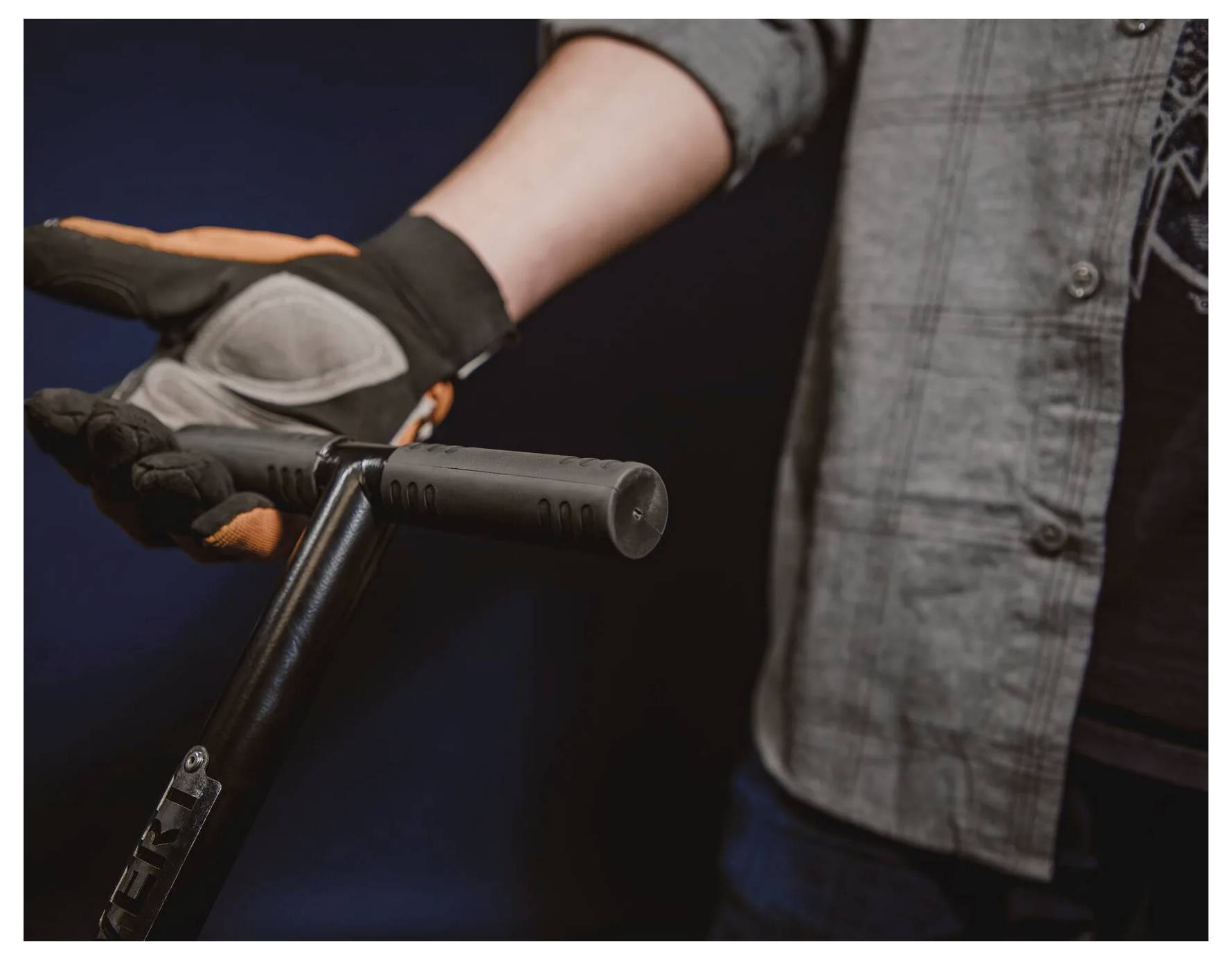 Eine Person mit Handschuhen hält den Lenker eines Rollers. Der Fokus liegt auf den Händen und dem Lenker vor einem dunklen Hintergrund.