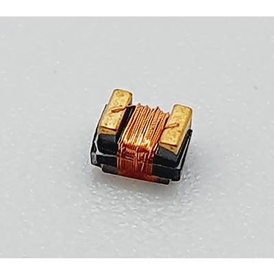 Eine kleine elektronische Komponente mit um einen schwarzen Kern gewickeltem Kupferdraht, die auf einer hellgrauen Oberfläche platziert ist.