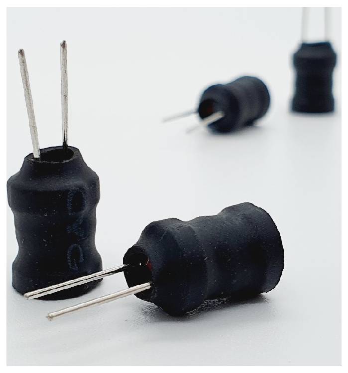 Nahaufnahme von vier schwarzen zylindrischen elektronischen Bauteilen mit Metallpins auf einer weißen Oberfläche, höchstwahrscheinlich Induktoren oder Kondensatoren.