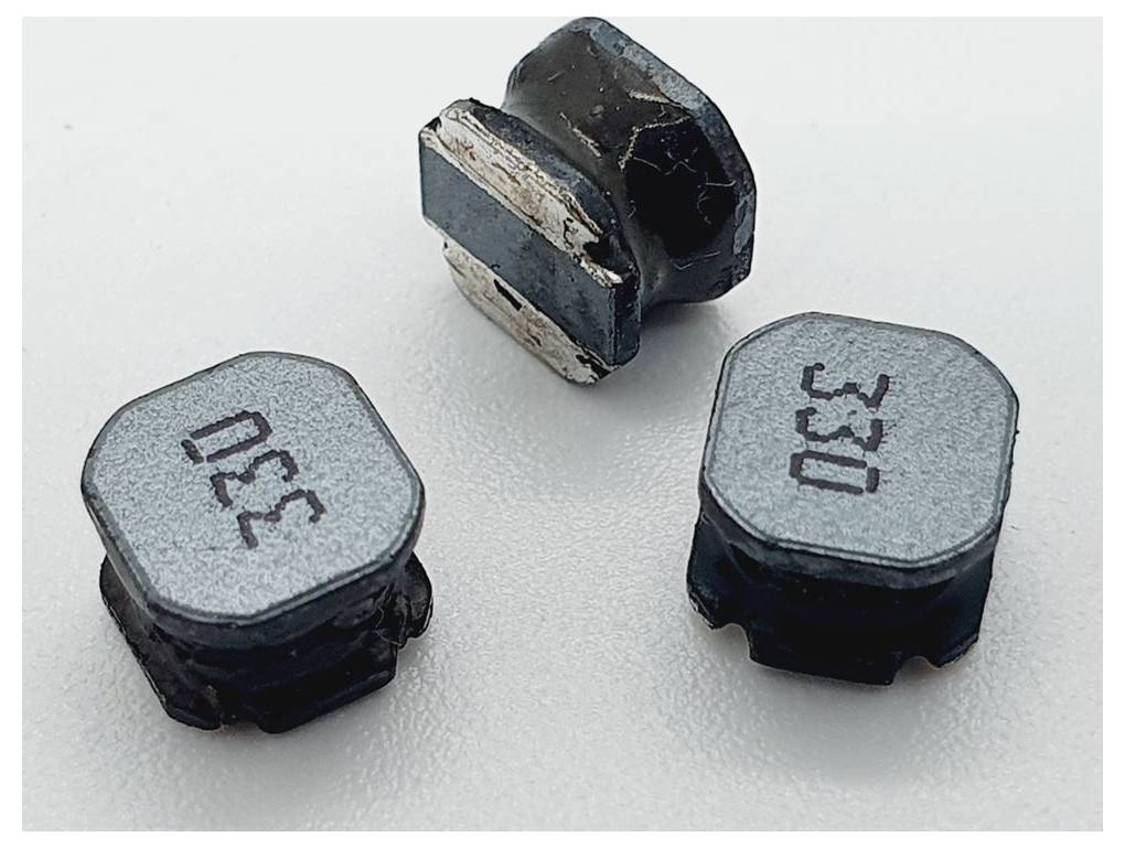 Drei beschädigte elektronische Komponenten, mit dem Etikett '330', ruhen auf einer hellen Oberfläche. Eine steht aufrecht und zeigt sichtbare Abnutzungsspuren, während die anderen flach liegen.
