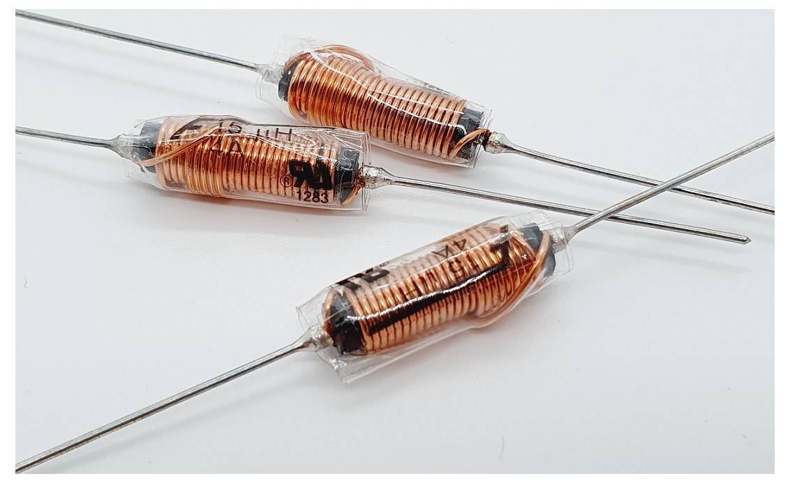 Drei orange-gestreifte zylindrische Induktoren mit Metallanschlüssen, parallel auf weißem Hintergrund angeordnet, verwendet in elektronischen Schaltkreisen.