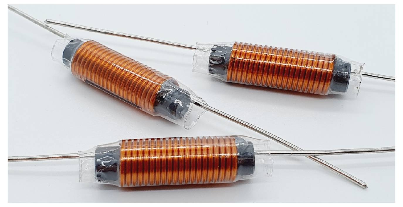 Drei orange zylindrische elektrische Komponenten mit Anschlussdrähten, höchstwahrscheinlich Induktoren, auf einem weißen Hintergrund.