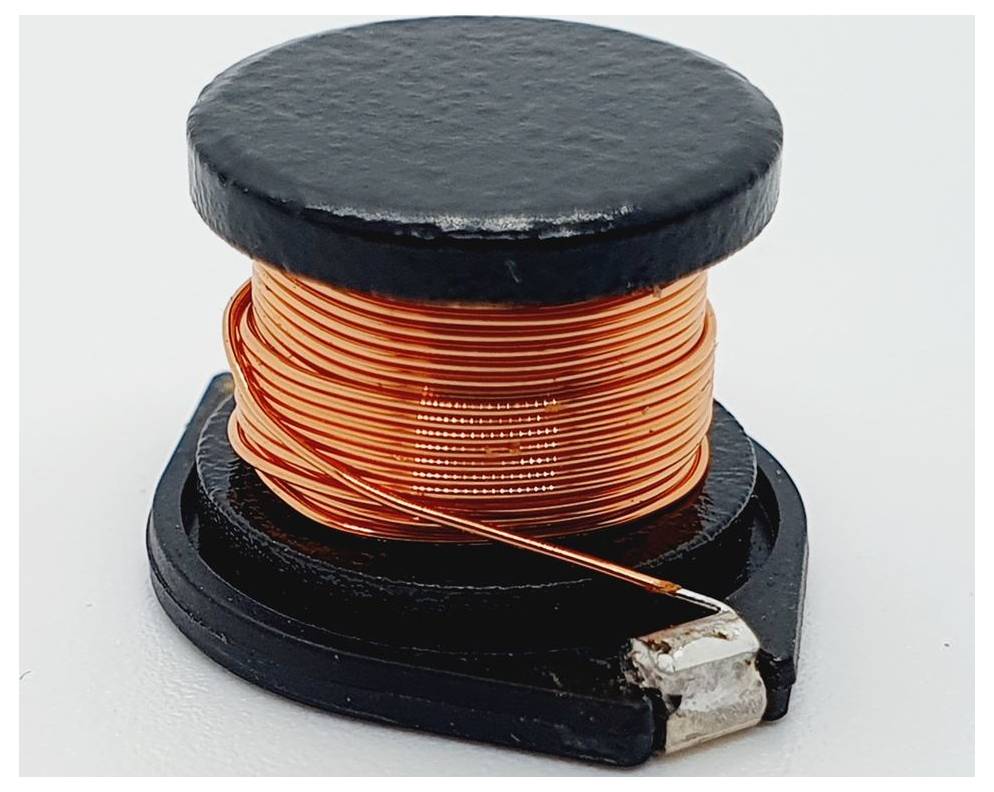 Eine Spule aus Kupferdraht, die um eine schwarze kreisförmige Basis gewickelt ist, mit einem kleinen metallischen Anschluss an einem Ende, verwendet in der Elektronik.