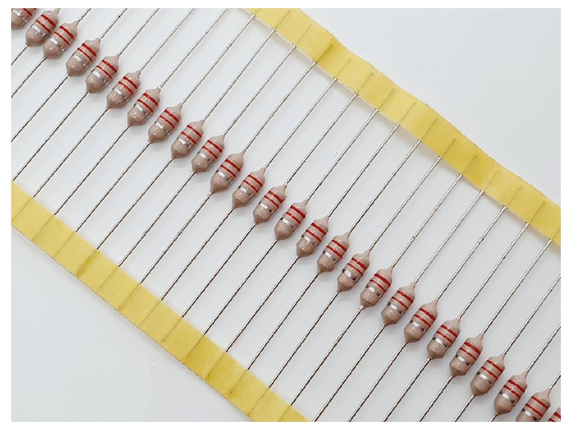 Eine Reihe identischer Widerstände mit roten und goldenen Ringen, die auf einem gelben Band montiert sind und ihren Widerstandswert anzeigen.